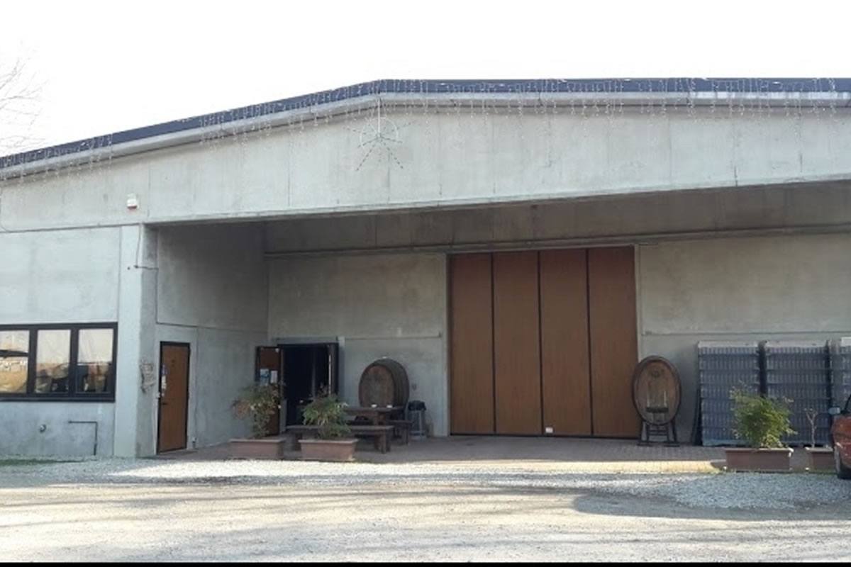 Edificio industriale in cemento con porta a soffietto in legno. Ingresso con tavoli e botti. Azienda agricola Gruppo Vignaioli.