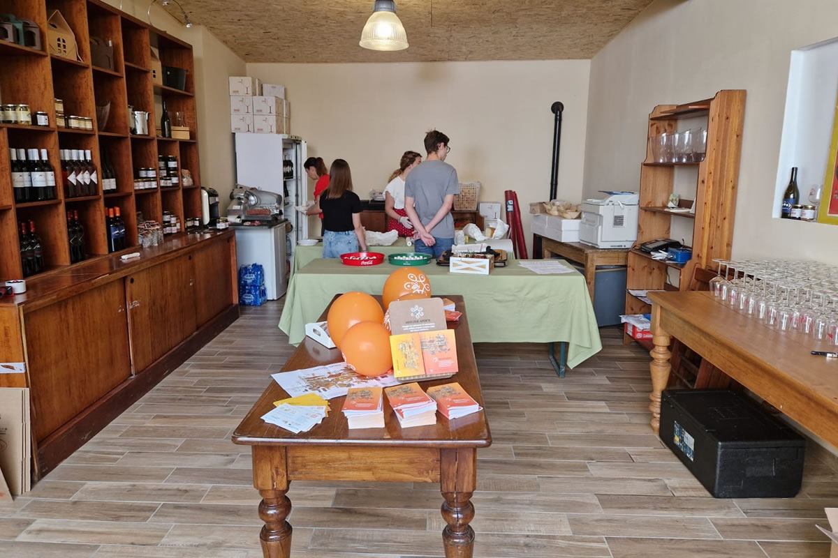 Negozio di alimentari con scaffali in legno, bottiglie, persone al bancone e tavoli con prodotti. Azienda agricola I Germogli.