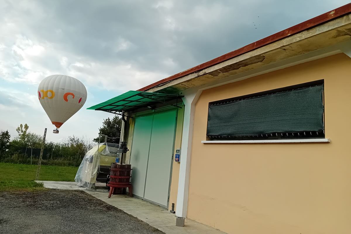 Mongolfiera bianca e gialla in volo sopra un edificio giallo con finestra oscurata. Azienda agricola, cielo nuvoloso.
