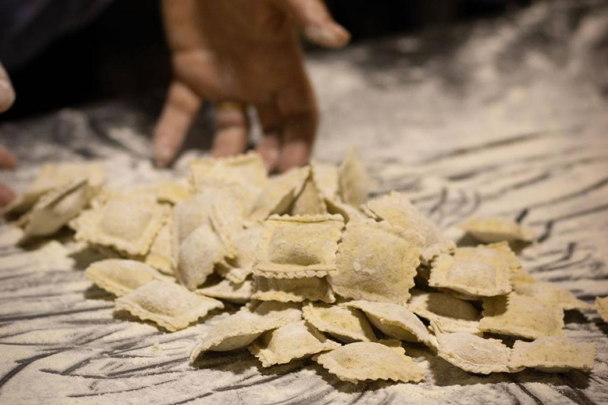 Ravioli fatti a mano su un tavolo infarinato. Una mano si avvicina ai ravioli. Pasta fresca, cucina italiana.