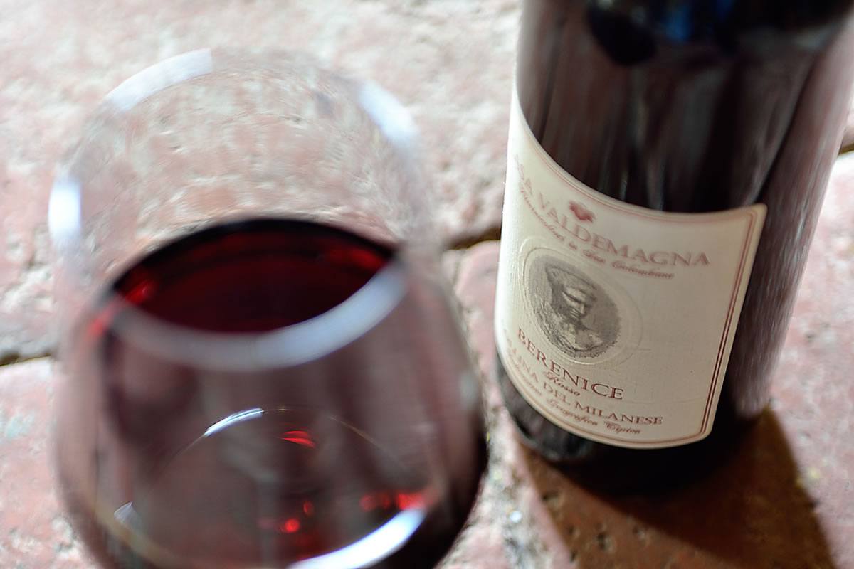 Bicchiere di vino rosso e bottiglia di Casa Valdemagna Berenice su superficie in pietra.