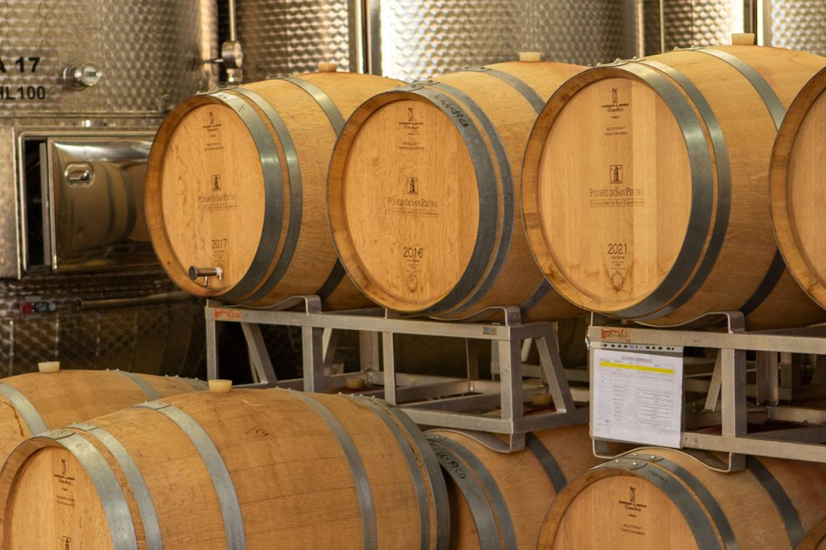 Botti di vino in legno con cerchi metallici, etichette Poderi San Pietro, annate 2016, 2017, 2021. Cantina, produzione vino.