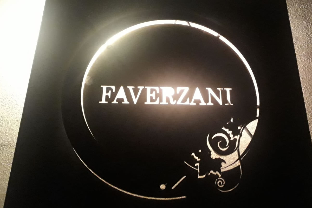 Logo Faverzani. Cerchio nero con scritta bianca Faverzani illuminata. Decorazioni floreali stilizzate.